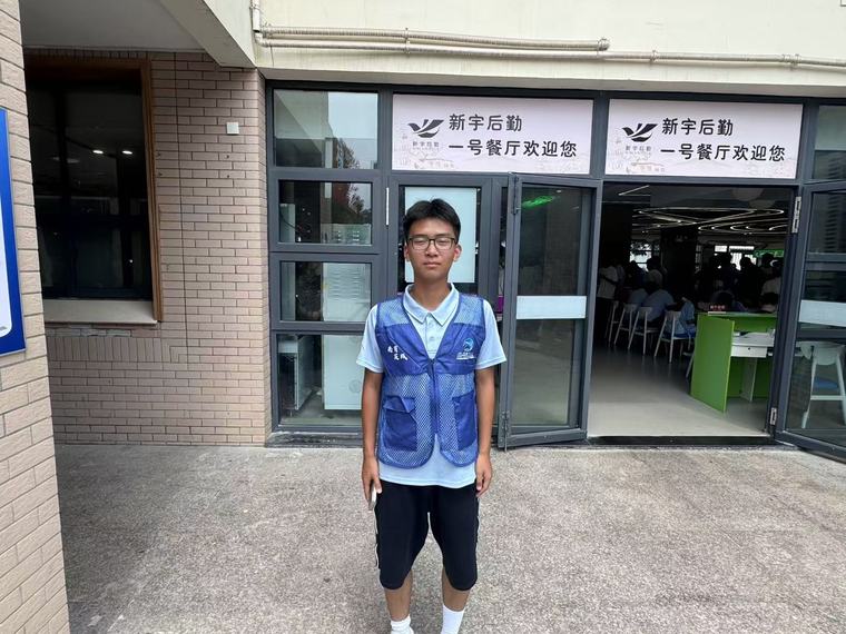 一位戴眼镜的同学站在一号餐厅门口