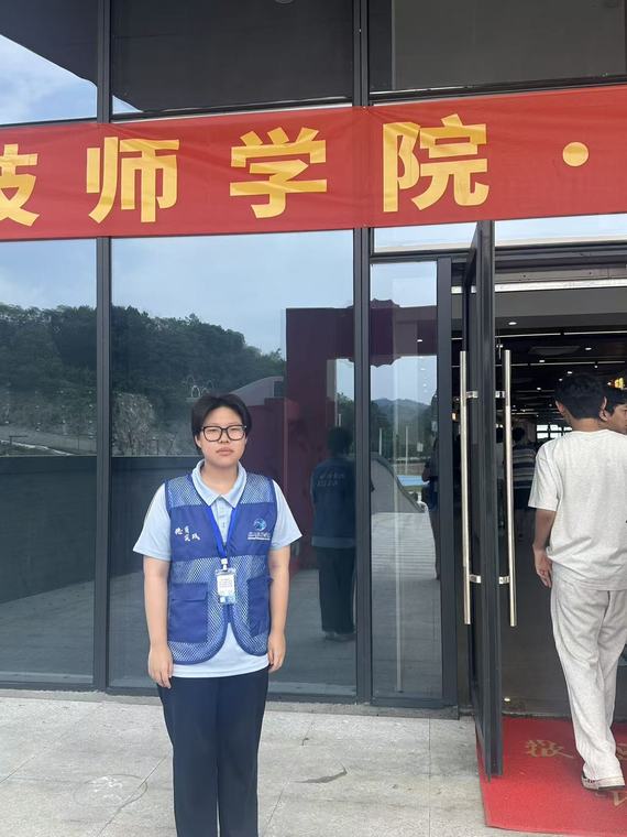 一位戴眼镜的同学站在写有技师学院字样的红色横幅下
