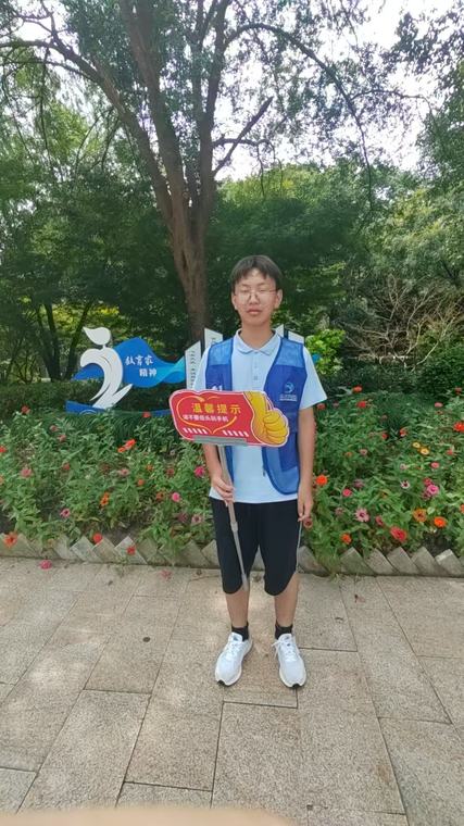 一位同学在花坛前举着红色提示牌