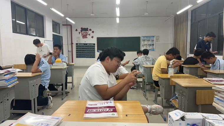 教室里同学们坐在课桌旁，有人在看手机，有人在聊天