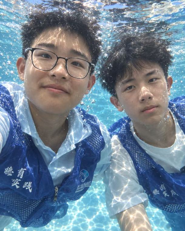 两位同学在泳池水下自拍，穿着蓝色马甲