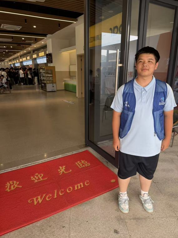 一位同学站在写有欢迎光临 Welcome 的红色地垫上